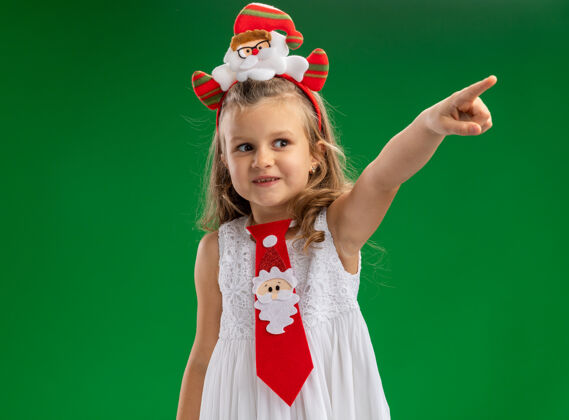 穿令人印象深刻的一面看小女孩戴着圣诞发箍与领带点在一边孤立的绿色墙壁箍领带分