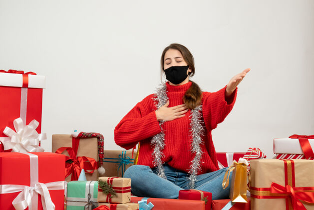 礼物穿着红色毛衣 戴着黑色面具的年轻女孩张开手闭上眼睛围坐在白色的礼物上女孩圣诞节眼睛