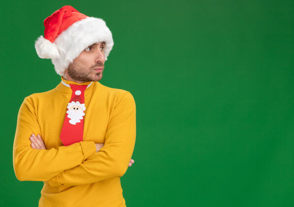 体贴体贴的年轻白人男子戴着圣诞帽 打着领带 站在那里 用封闭的姿势看着被隔离在绿色背景上的一边 还有复制空间领带侧看