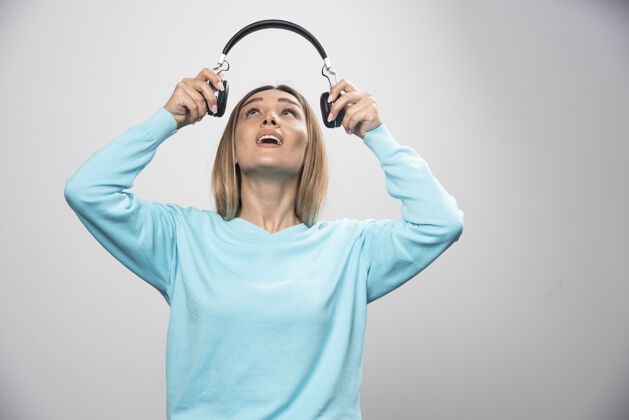 积极穿着蓝色运动衫的金发女孩拿着耳机 准备戴上耳机听音乐成人娱乐休闲