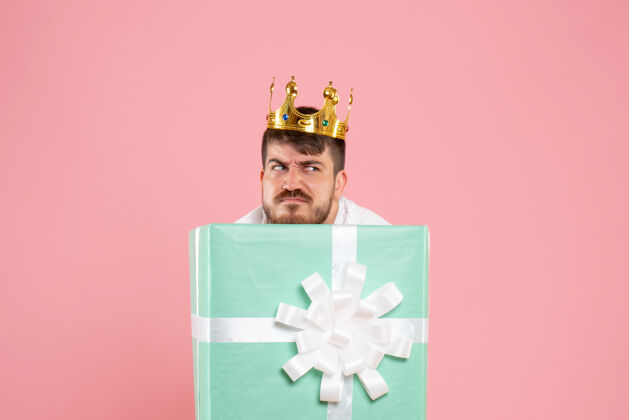 盒子年轻人在礼物盒内的正面视图 浅粉色墙上有皇冠里面人年轻