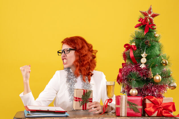 背景前视图：女医生坐在桌子后面 黄色背景上有圣诞礼物成人情感桌子