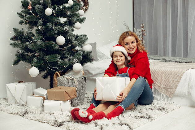 牛仔裤人们在为圣诞节做准备母亲在和女儿玩耍一家人在节日的房间里休息孩子穿着红色毛衣家庭礼物帽子