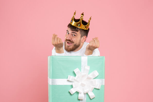 男性年轻人在礼物盒内的正面视图 粉红色墙上有皇冠正面情感年轻