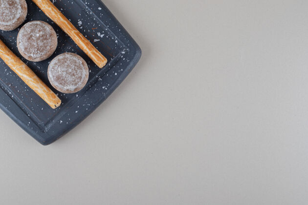 香料把小饼干和饼干放在大理石背景上的海军蓝盘子上烘焙板棒