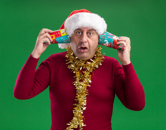 绿色中年男子戴着圣诞老人帽子 脖子上戴着金属丝 手里拿着五颜六色的纸杯戴着圣诞老人看