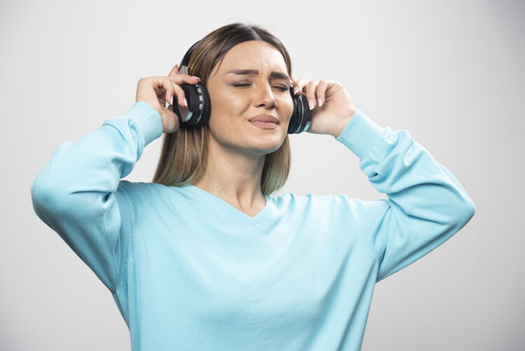 摆姿势穿着蓝色运动衫的金发女孩戴着耳机 享受着音乐和乐趣女人音乐年轻