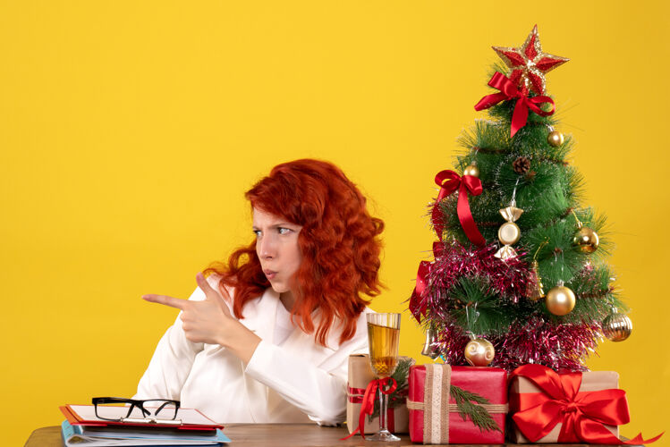 圣诞节女工人坐在桌子后面 拿着圣诞树和黄色的礼物黄色工人女