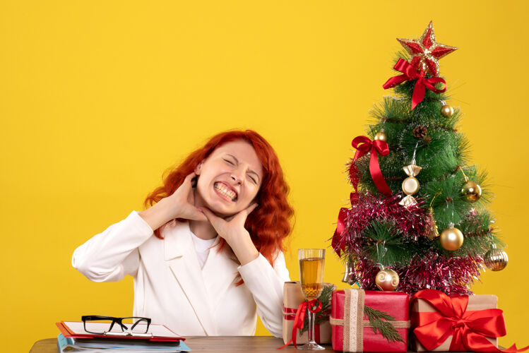 黄色女工人坐在桌子后面 手里拿着圣诞礼物和黄色的圣诞树安排坐着礼物