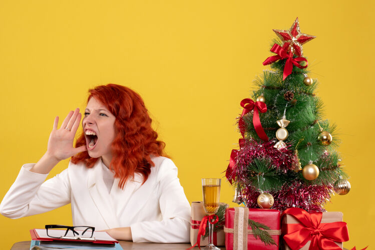 工人女工人坐在桌子后面 拿着圣诞树和黄色的礼物尖叫桌子办公室圣诞节