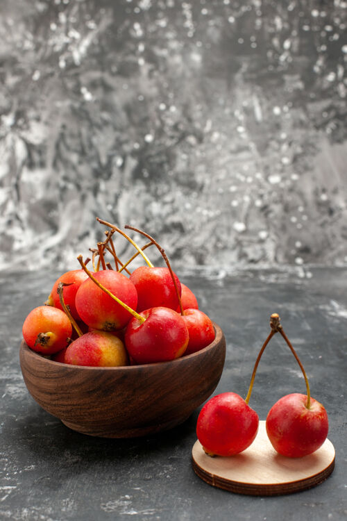 木制红色的樱桃在棕色的碗里和灰色的小木托盘上的垂直视图浆果灰色甜点