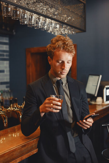 男人自信开朗的男人坐在吧台旁 喝着啤酒 用智能手机上网玻璃技术电话