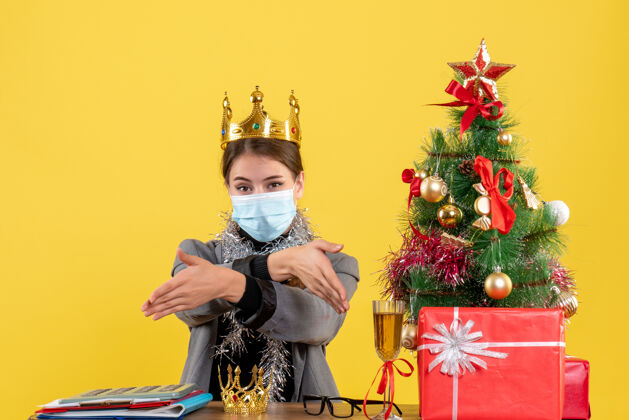 礼物正面图戴着医疗面罩戴着皇冠的年轻女孩手拿圣诞树和鸡尾酒树表演者穿着