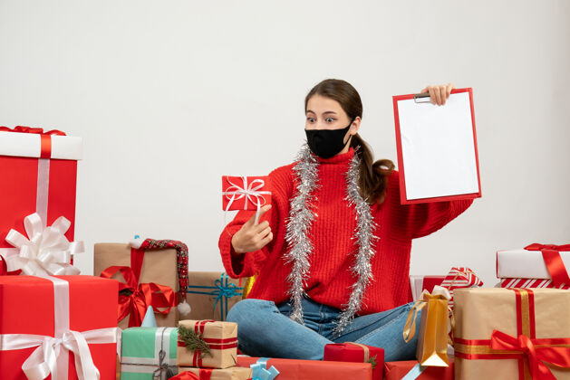 人带着黑色面具拿着文件和礼物的惊讶女孩围坐在白色的礼物上圣诞节惊讶礼物