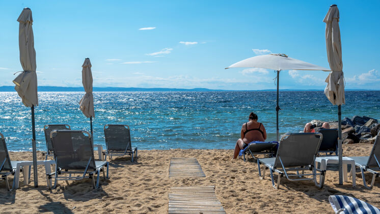 希腊在希腊尼基提 爱琴海海岸的海滩上有雨伞和日光浴床 休息的情侣 靠近水面的岩石风景雨伞海湾