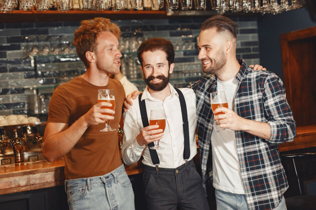 年轻和最好的朋友见面三个穿着休闲服的快乐的年轻人一起坐在酒吧里聊天喝啤酒足球友谊放松