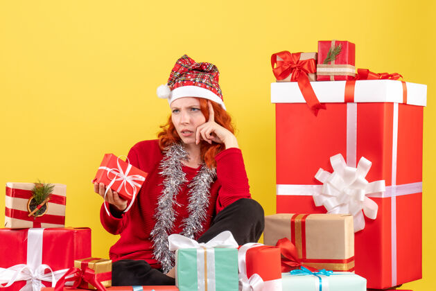 人坐在黄色墙上的圣诞礼物周围的年轻女子的正视图庆祝帽子礼物
