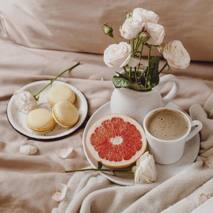 麦卡龙一束鲜花 床上放着咖啡和葡萄柚方形小吃美食