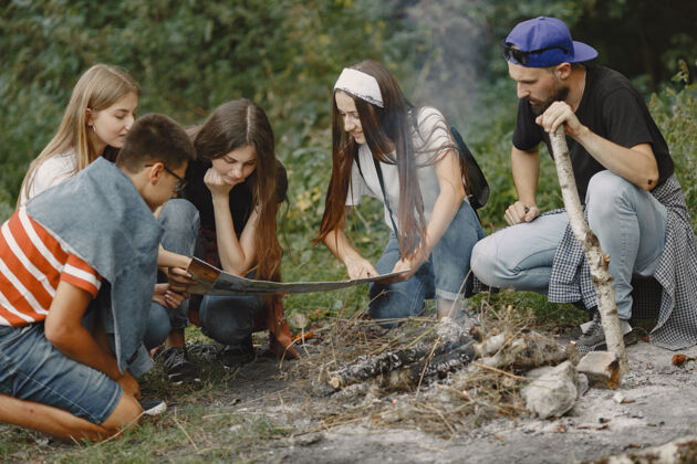 冒险探险 旅游 远足和人的概念一群微笑的朋友在森林里人们坐在篝火旁放松森林旅游
