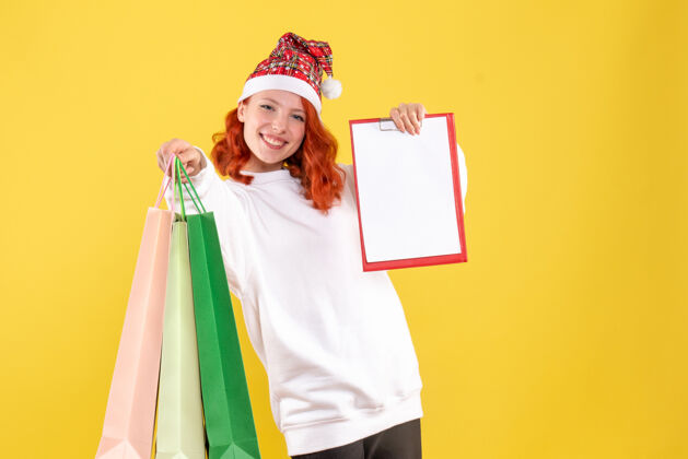 包黄色墙壁上拿着购物包的年轻女子的正视图快乐快乐商场