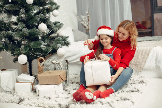 毛衣人们在为圣诞节做准备母亲在和女儿玩耍一家人在节日的房间里休息孩子穿着红色毛衣给予节日花环