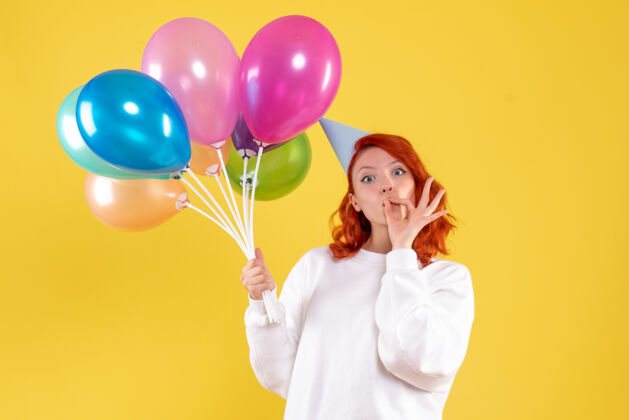 气球黄色墙壁上手持可爱彩色气球的年轻女子的正视图快乐女人情感