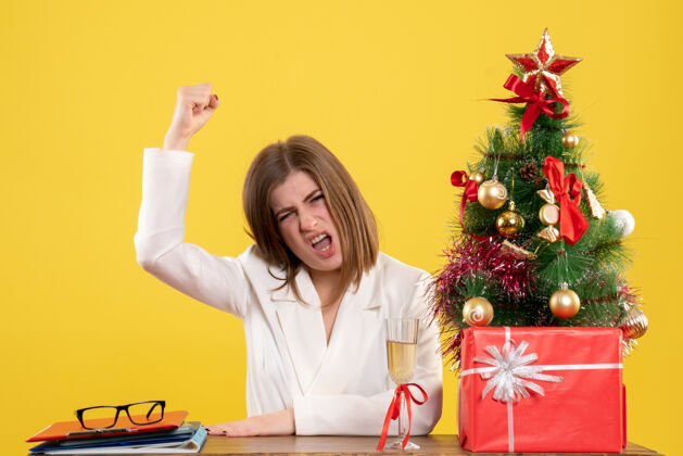 背景正面图：女医生坐在黄色背景的桌子前 放着圣诞树和礼品盒电脑前面年