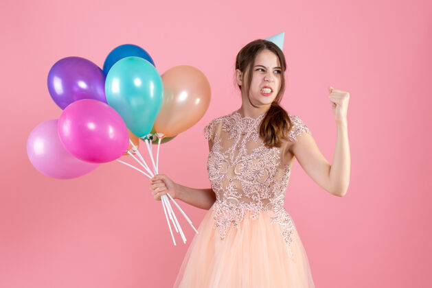 愤怒戴着派对帽拿着气球的派对女孩对粉色的东西很生气聚会庆祝粉红色