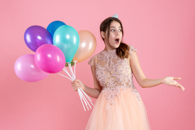 肖像带着派对帽的惊喜派对女孩拿着粉色的气球时尚举行公主
