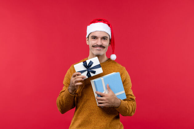 人红墙上拿礼物的年轻人的正面图举行圣诞节前面