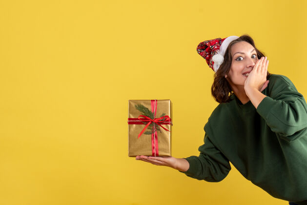 Covid黄色墙上拿着小圣诞礼物的年轻女子的正视图人前面抱