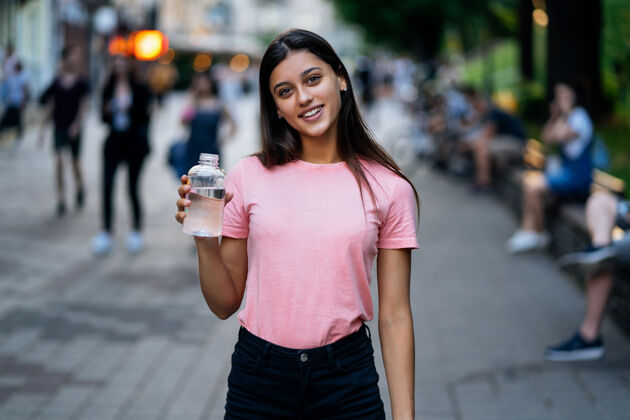 举行美丽的年轻女孩在城市的街道上拿着一瓶水年轻欧洲快乐