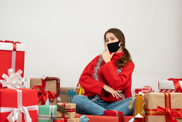 成人穿着红色毛衣 戴着黑色面具的年轻女孩正在做手指枪的手势 围坐在白色的礼物上人们圣诞节毛衣
