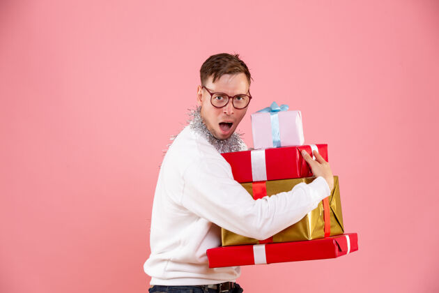 盒子在粉红色墙上拿着圣诞礼物的年轻人的正视图举行假日年轻男性