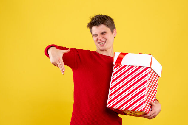 举行黄色墙上拿着圣诞礼物的年轻人的正视图微笑礼物盒快乐