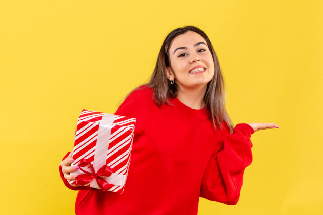 快乐黄色墙上年轻女子微笑着拿着圣诞礼物的正面图举行前面庆祝