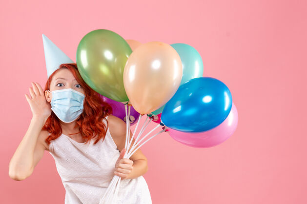 女性前视图中的年轻女子拿着五颜六色的气球在无菌面具上粉红色的墙壁年轻前无菌