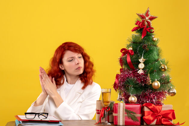 安排女工人坐在桌子后面 手里拿着圣诞礼物和黄色的圣诞树圣诞女情感