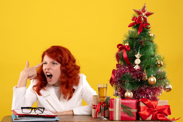 漂亮女工人坐在桌子后面 手里拿着圣诞礼物和黄色的圣诞树办公室桌子女