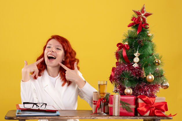 黄色女工人坐在桌子后面 拿着圣诞树和黄色的礼物人女工人