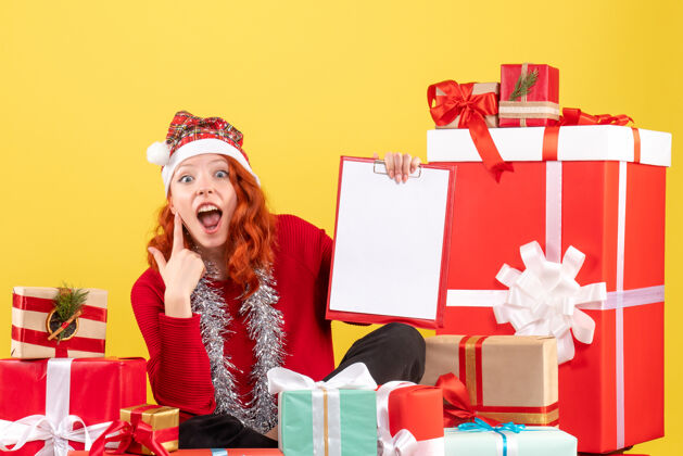 购物年轻女子围坐在黄色墙壁上的不同圣诞礼物前视图礼物节日盒子