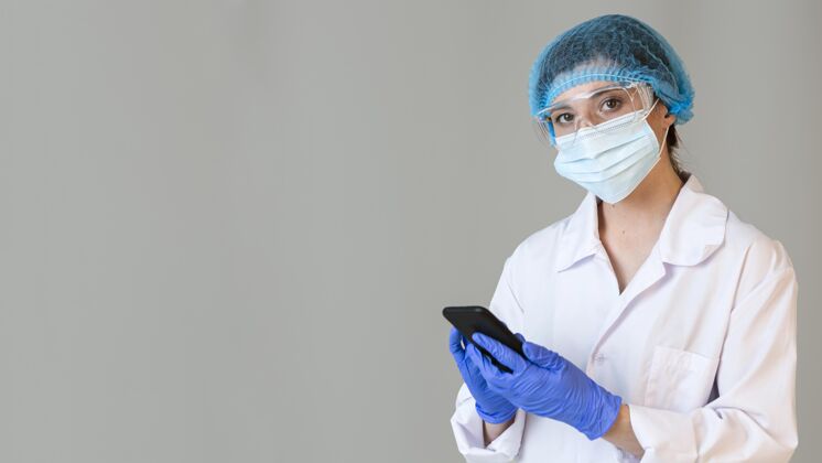 女人戴着安全眼镜和医用面罩手持智能手机的女科学家检查手套研究