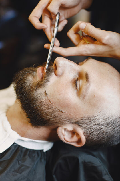 肖像有胡子的男人有客户的理发师有梳子和剪刀的男人理发师剪时尚