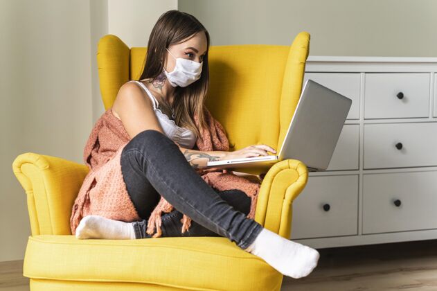 Ncov大流行期间 戴着医用口罩的妇女坐在扶手椅上操作笔记本电脑家庭预防扶手椅