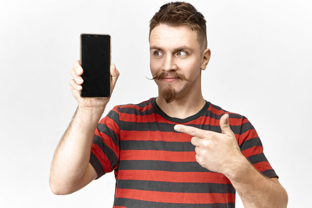 持有看看这个年轻帅气 情绪化的推销员 留着时髦的胡须 留着小胡子 手里拿着智能手机 用食指指着空白的屏幕 展示着这个小玩意儿演示电话显示