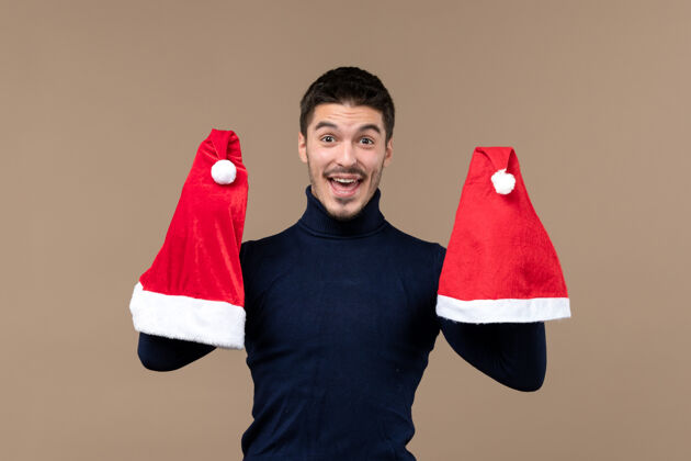 圣诞节正面图：年轻男性在棕色背景上玩红色帽子圣诞情绪新年衣服红色长袜