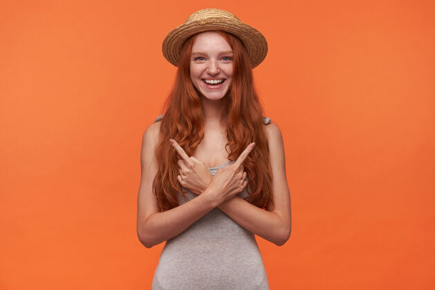 波浪快乐的年轻美丽的狐狸长发女士穿着休闲服在橙色背景上摆姿势的室内照片 用抬起的食指指向不同的方向 积极的情绪概念肖像手指女性