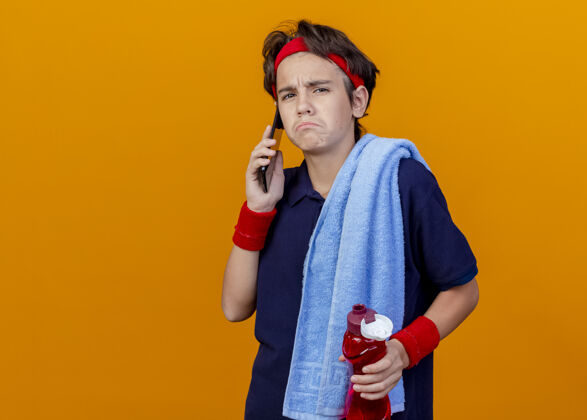 运动悲伤的年轻帅气的运动男孩 肩上扛着毛巾 手里拿着水瓶 一边打电话帅气毛巾说话