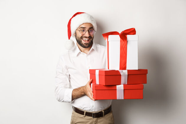 兴奋寒假和庆祝快乐的家伙带来圣诞礼物 拿着礼物 戴着圣诞帽 站着圣诞老人帽子冬天