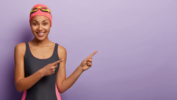 浴衣健康的女游泳运动员戴泳帽和护目镜 用食指指向一边游泳运动女性